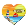 Magnes w kształcie serca przedstawiający latarnię i kuter na tle zachodzącego słońca.
