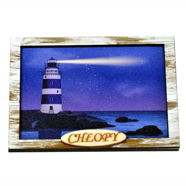 Pamiątka znad morza przedstawiająca świecącą w nocy latarnię morską stojącą na kamieniach na brzegu morza.