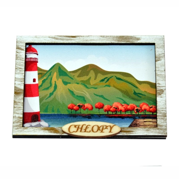 Magnes z biało czerwoną latarnią i górami w tle. Posiada pozłacaną ręcznie malowaną ramkę oraz napis miejscowości.